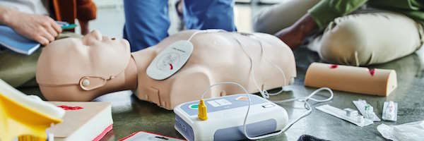 Frontline CPR AED First-Aid-1 CPR manikin, defibrillator, wound care simulators, compression tourniquet, bandages and syringes near instructor and multiethnic participants of first aid seminar, emergency preparedness concept
